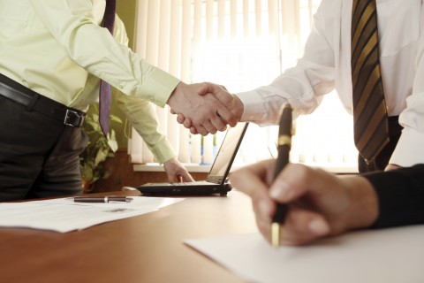 Papers being Signed while Two Businessmen Shake Hands on a Deal