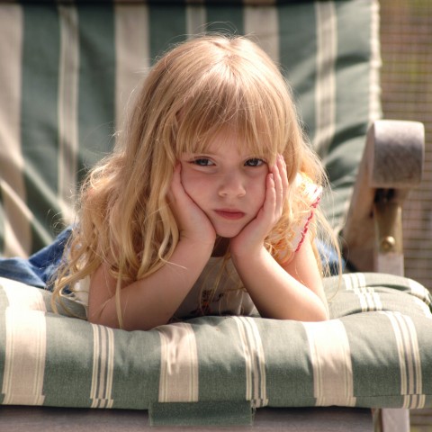 A Little Girl Sitting on Outdoor Furniture with an Unhappy Look on Her Face