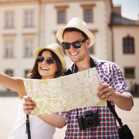 Young Tourist Couple with Hats and Sunglasses on, Studying a Map