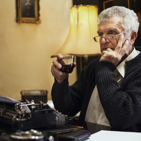 Pensive Author in Front of Old Typewriter, Sipping a Drink