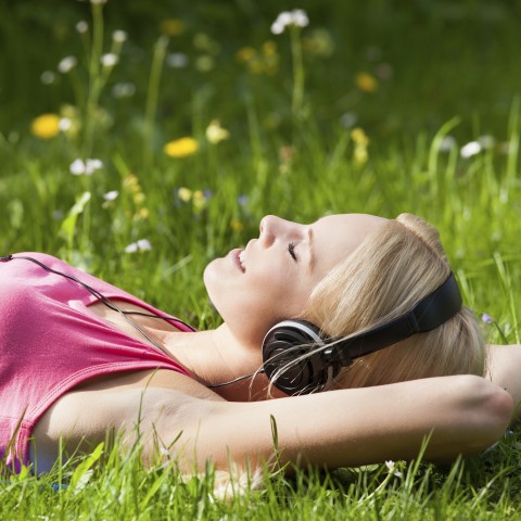 A Woman Lying Down in the Grass with Headphones on and a Smile on Her Face