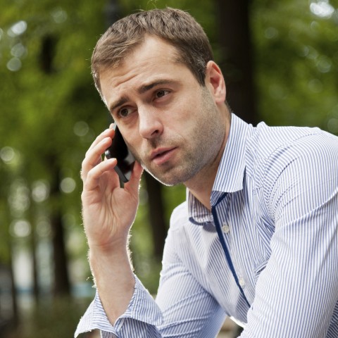 A Young Man Sitting Outside, Talking on a Cellphone.