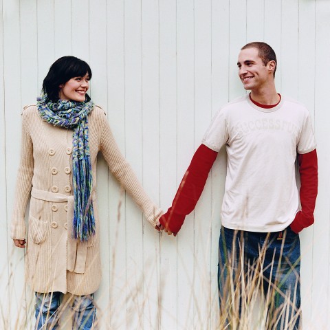 Couple Holding Hands in Front of a White Wall, Smiling at Each Other