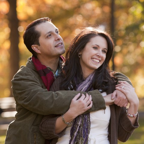 A Man with Arms Around His Wife as They Stand in a Park During Autumn 