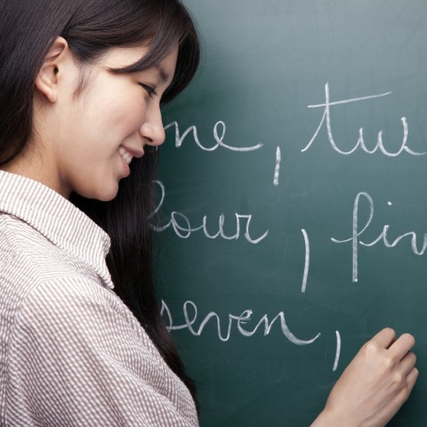 Female Tutor or Teacher Writing Words on a Board with White Chalk