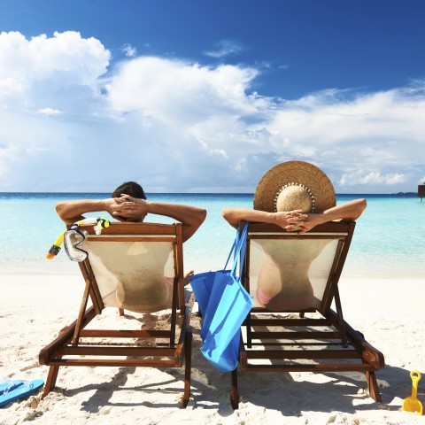 A Rear View of Couple Sitting on Deck Chairs on the Beach