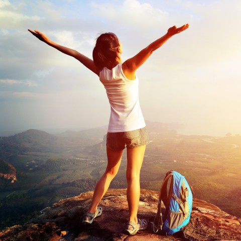 A Woman Raising Her Arms in Victory Atop a Mountain