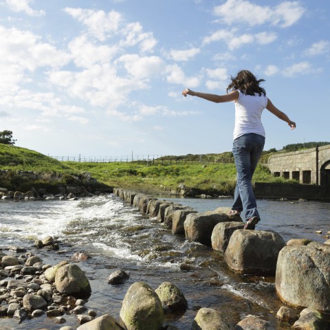 A Woman Walking on Stones Over a River