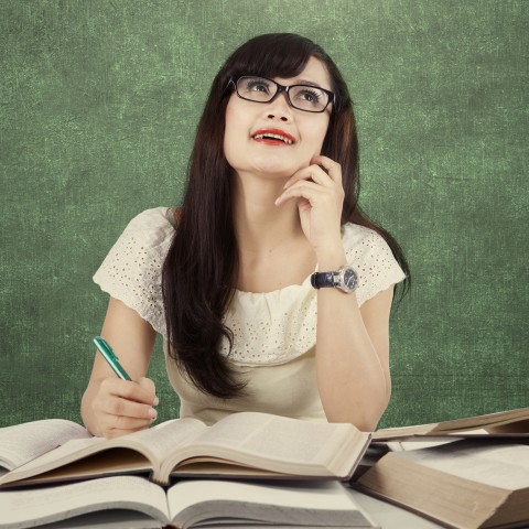 A Woman Sitting in Front of a Blackboard, Studying Books, and Looking Up to Think