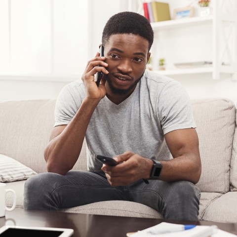 A Guy Talking on the Phone while Watching TV with a Remote in His Hand