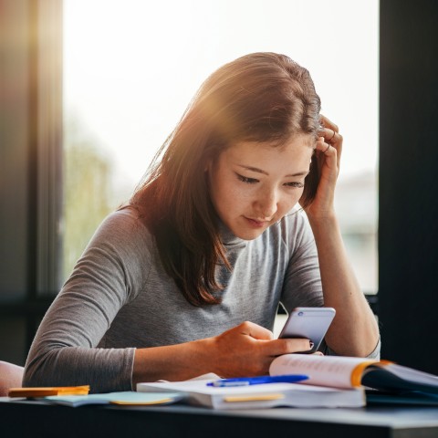 A Woman Studying with Her Phone and a Textbook