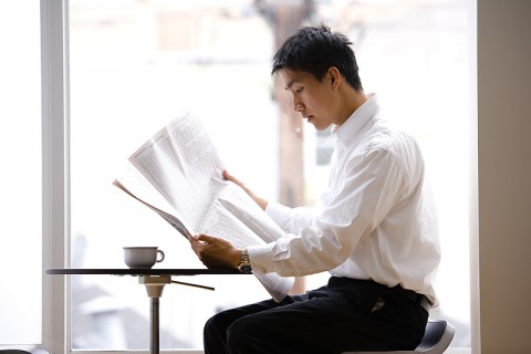 A Japanese Man Reading a Newspaper by a Large Window