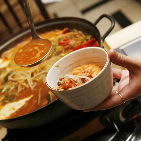 A lady holding a bowl of Kimchi soup