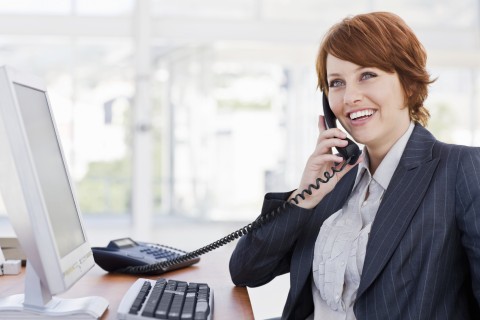 A Friendly Young Businesswoman Talking on a Telephone at Her Desk.