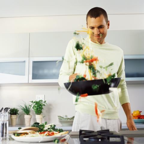 Man in a kitchen, tossing food in a wok