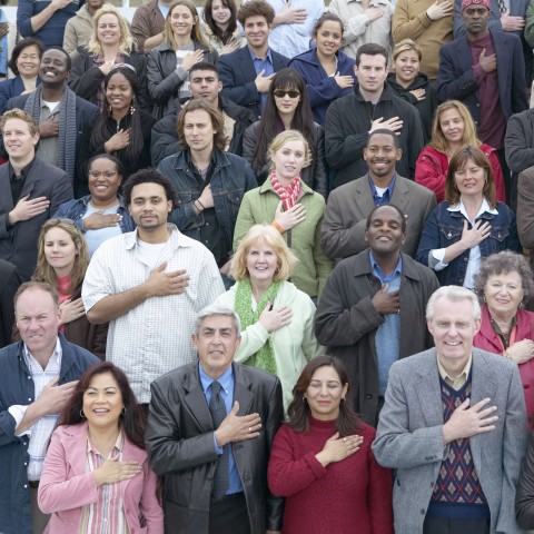 A Crowd of People Smiling with Their Right Palms Placed Over the Left Side of Their Chests.