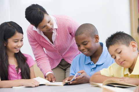 Three Students Studying in a Classroom with a Teacher Standing Nearby