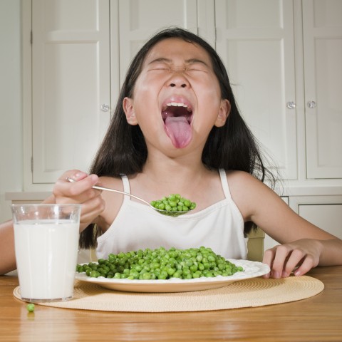 A Little Girl Making a Disgusting Face While Eating Peas