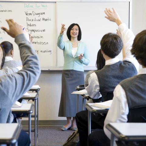 Teacher in the Classroom with Students Raising Their Hands