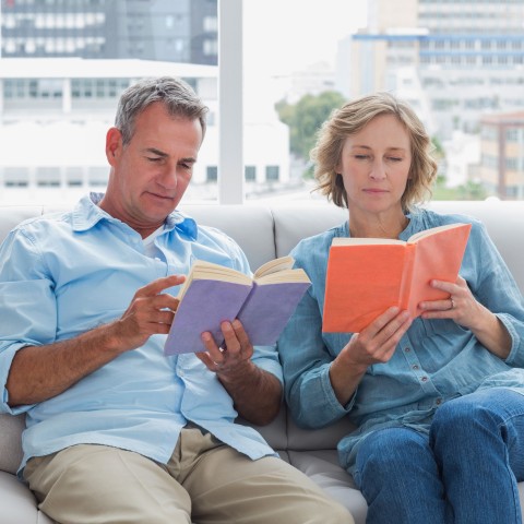 A Couple Sitting on the Sofa Reading Together