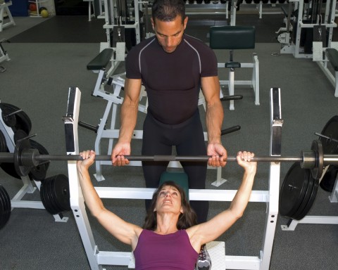 A Woman Weightlifting While Being Spotted by a Coach