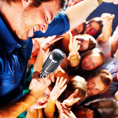 Singer Holding Mic Leaning Over His Swooning Audience