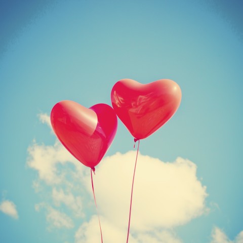 Two Heart-Shaped Balloons Floating against a Blue, Slightly Cloudy Sky