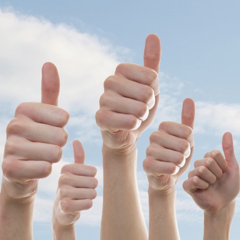 Five hands giving a thumbs up against a cloudy blue sky