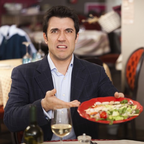 A Dissatisfied Customer Holding a Plate of Food in a Restaurant.