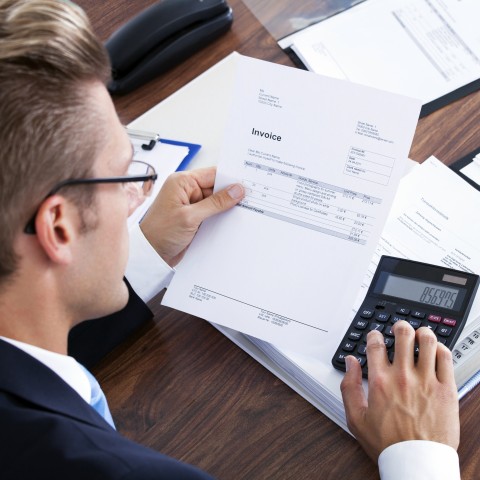 A Man Using a Calculator while Looking Over an Invoice Sheet