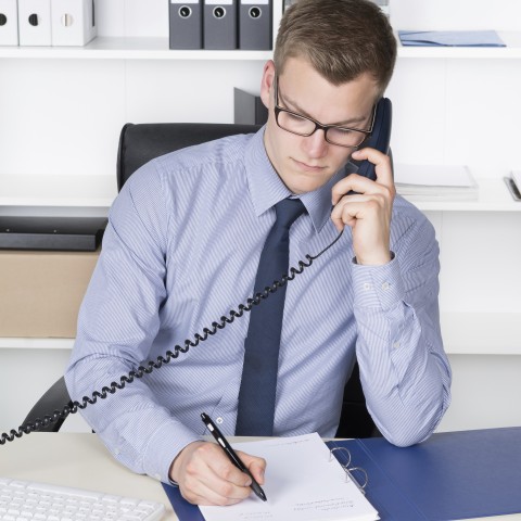 A Young Businessman Taking Notes During a Phone Call