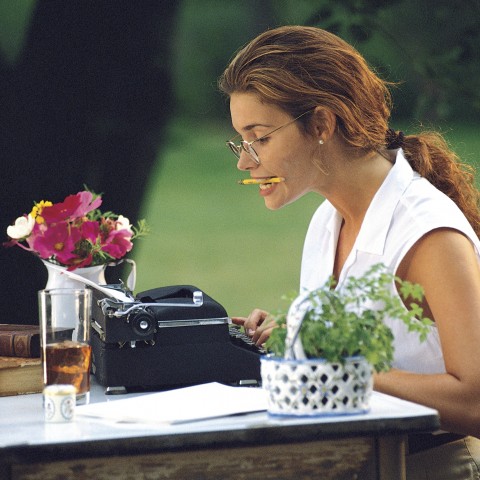 A Woman Writing Something at a Wooden Desk with a Typewriter