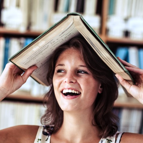 A Woman Smiling with a Book Over Her Head