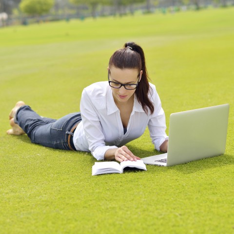 A Female Student on Campus Studying Outside with a Laptop and a Book