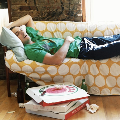 A Man Asleep on the Couch with Pizza Boxes and Beer Bottles Nearby