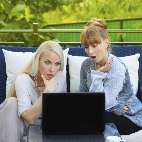 Две женщины смотрят на что-то на ноутбуке с удивлением на лицах