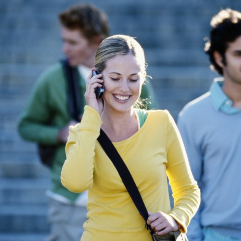 A Young Woman in a Yellow Top, Walking in the City while Talking on Her Cell Phone.