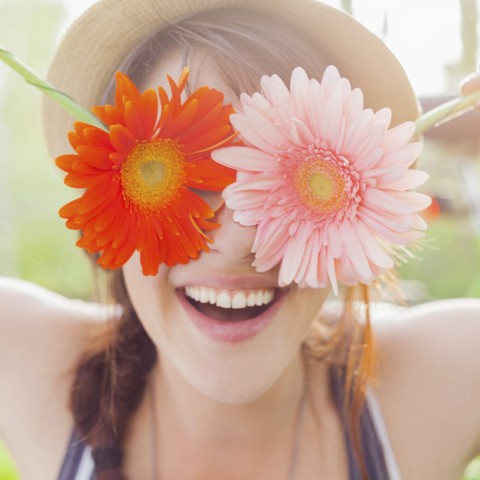 A Young Woman Smiling and Holding Flowers to Her Eyes