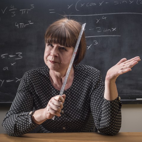 A Strict Teacher Sitting Behind Her Desk with a Ruler in Hand