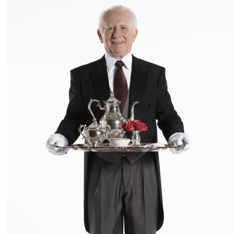 A Friendly, Elderly Butler in Formal Dress Holding a Smart Silver Tray and Tea Set