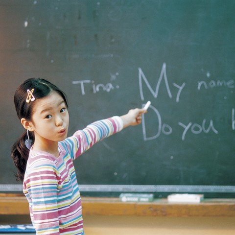 A Young Schoolgirl Introducing Herself to the Class in Front of a Blackboard.