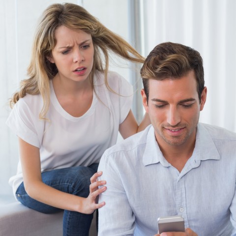 Woman Looking Over Partner’s Shoulder While He Texts