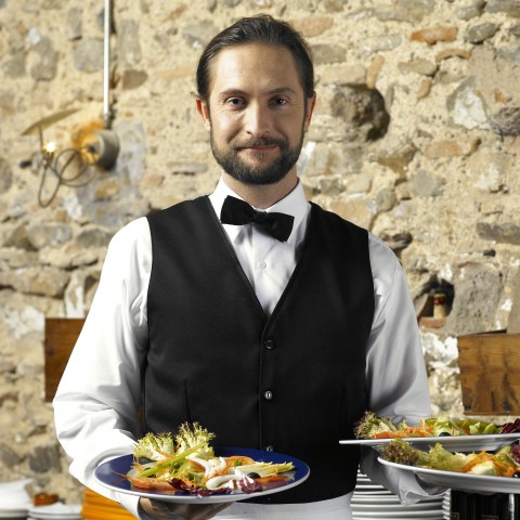 A Waiter in Formal Gear Holding Three Plates of Food.