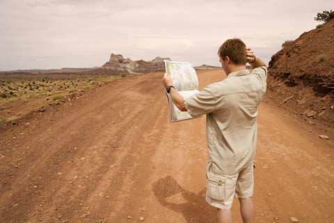 Man lost on a dusty road, looking at a road map and scratching his head