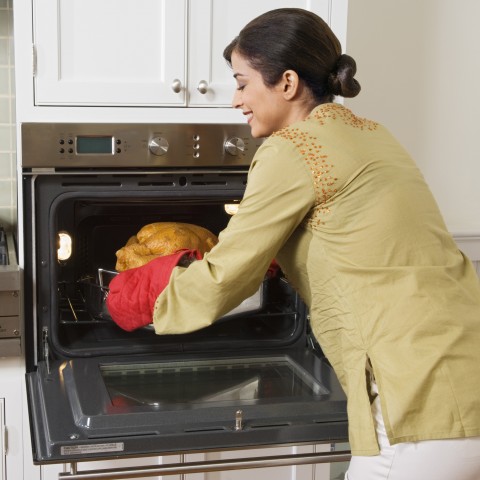 A Woman Taking a Whole Chicken Out of the Oven