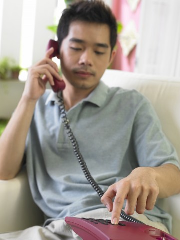 An Asian Man Pressing a Button while Talking on the Phone