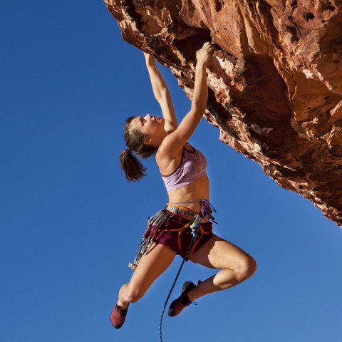 A woman rock climbing, hanging against a very blue sky.