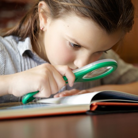 A Girl Reading a Book with the Help of a Magnifying Glass to Focus
