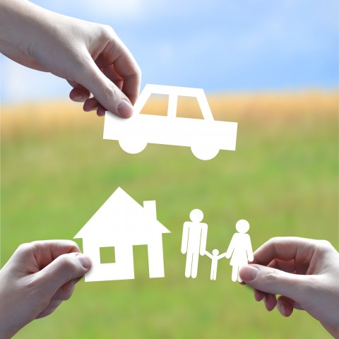 Three Hands Holding Paper Figures of a Family Setup - a House, Family Members, and a Car