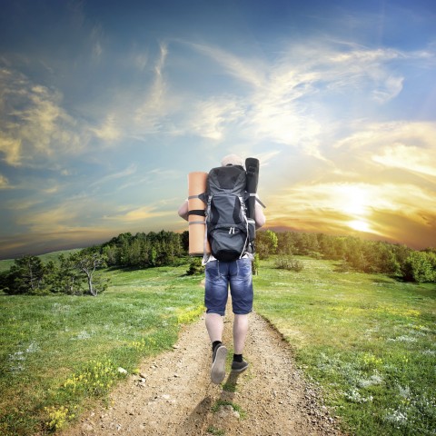 A Person with a Backpack Walking on a Path in Nature Towards Sunset